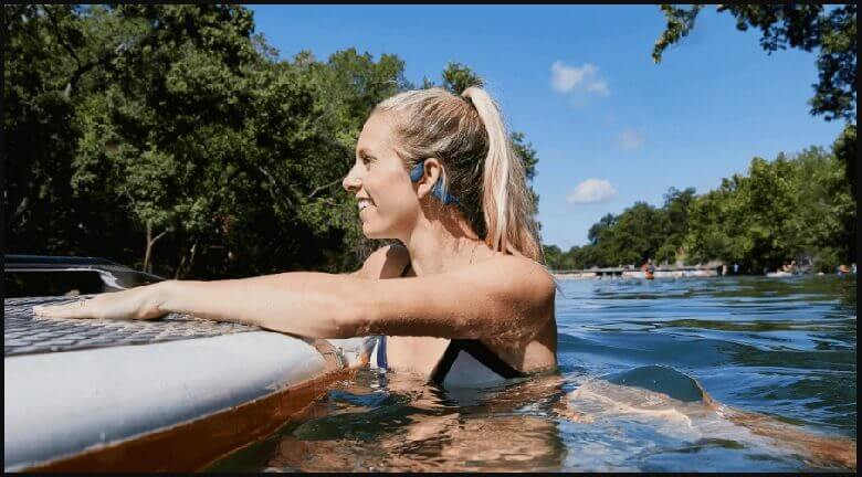 person wearing bone conduction headphones resting by a boat swimming in the open water