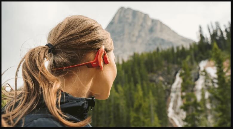 Adventurer using bone conduction headphones to enjoy music while hiking in a scenic landscape.