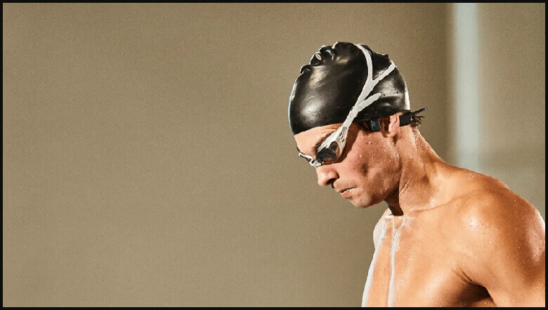 a man about to dive into the pool to swim with the shokz openswim bone conduction headphone and wearing a swim cap and swim goggle